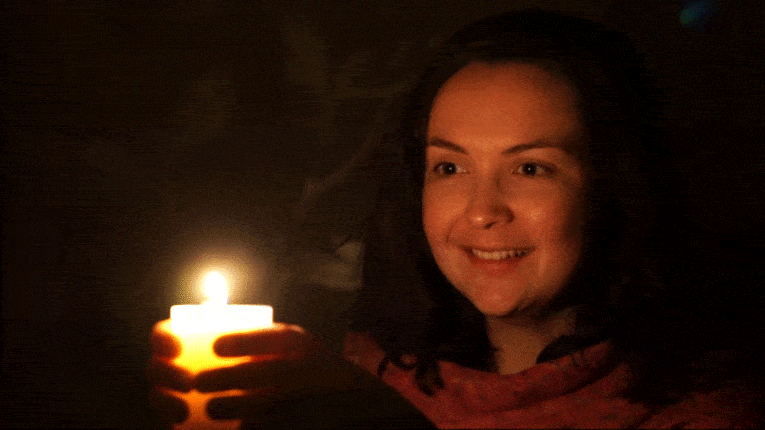 A cinemagraph showing a smiling woman holding a flickering candle